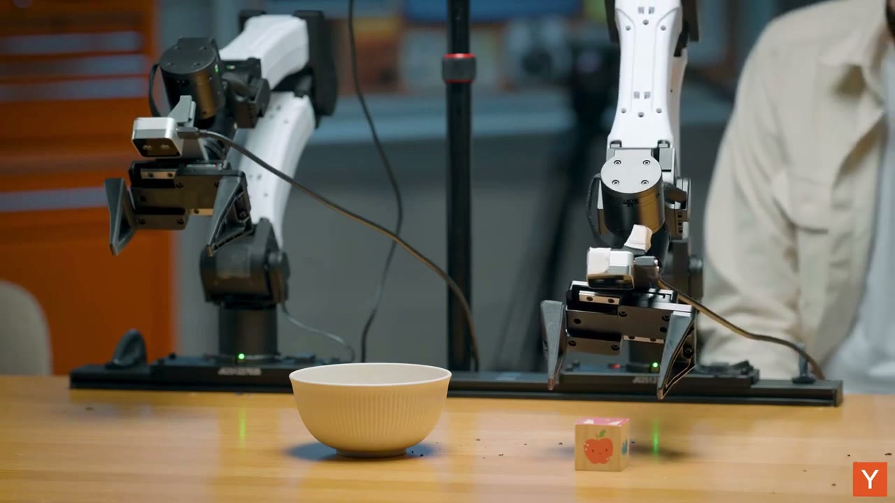 Two physical robot arms, a block and a bowl in the Y Combinator demonstration.